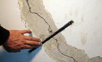 A wall with a large crack is being inspected by a professional in Baltimore, MD